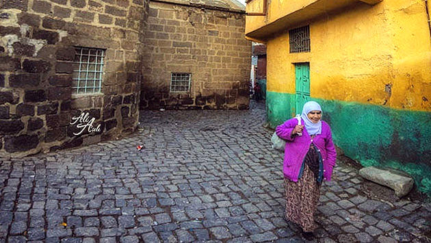 Diyarbakır Suriçi'nde sarı bir evin önünden geçen yaşlı kadın